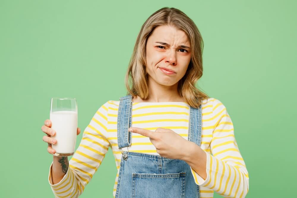 Mladenka sketično kaže s prstom na kozarec mleka v svoji drugi roki, nekaj je narobe z mlekom