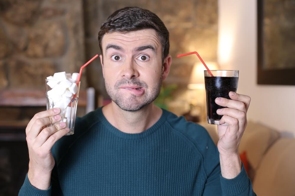 Mladenič s kozarcem polnim kock sladkorja v levi in s kozarcem kole v desni roki